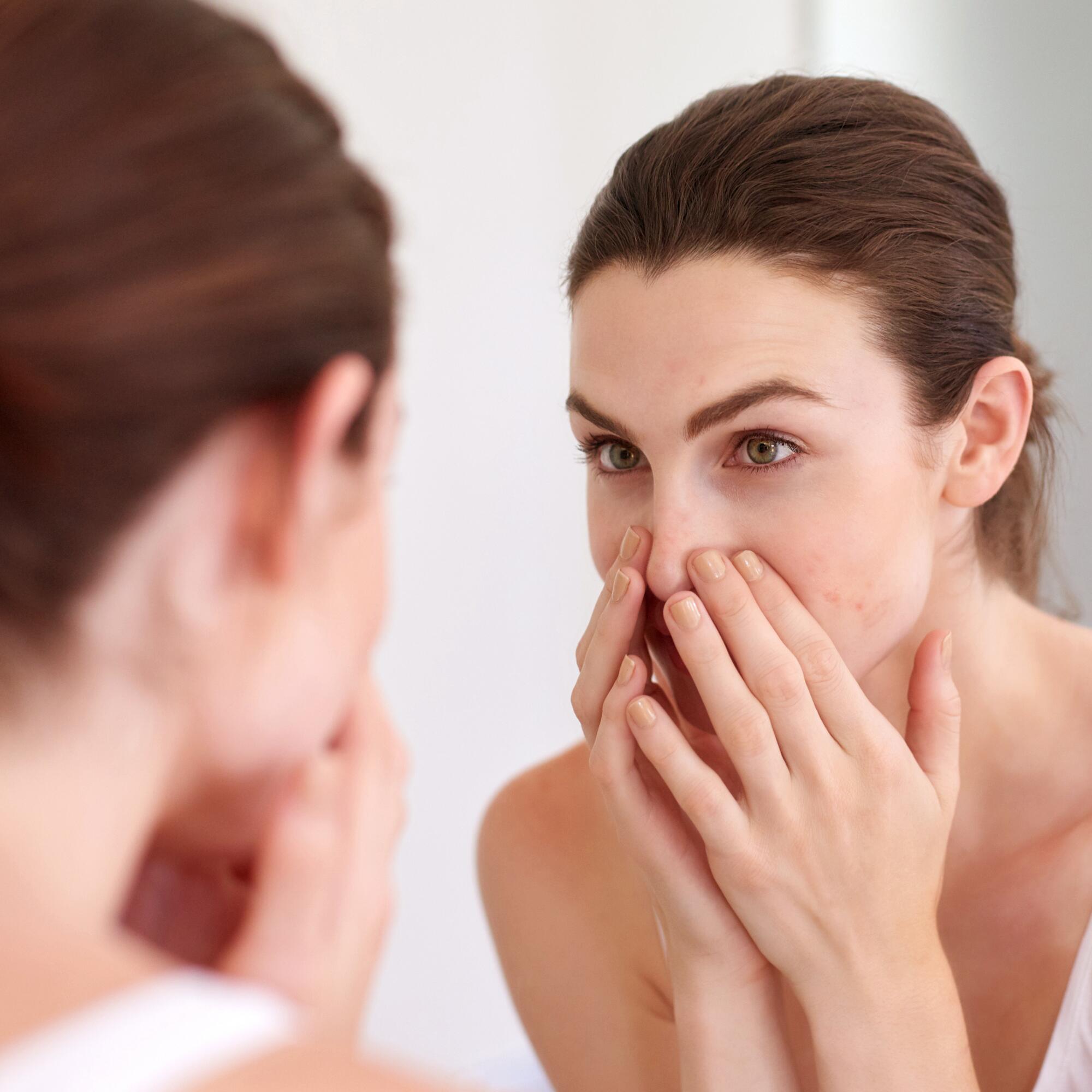 Eine Frau betrachtet ihre Nase im Spiegel und untersucht Mitesser im Gesicht.